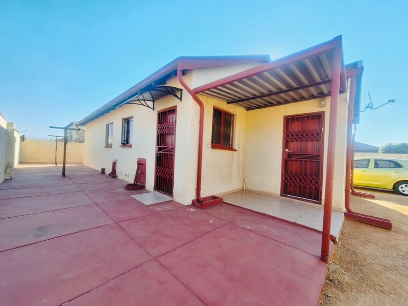 Rear exterior view of the house featuring a paved courtyard, covered patio area, and security gates on the entrances.