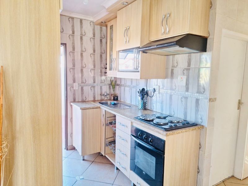 A compact kitchen featuring light wood-finish cabinetry, tiled backsplash, built-in oven, electric hob, and extractor fan with tiled flooring.