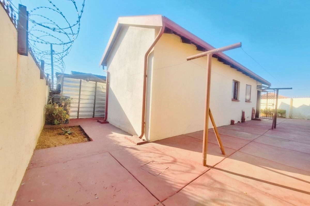 Rear exterior view of the property featuring a paved courtyard, perimeter wall with razor wire, and a metal storage shed.