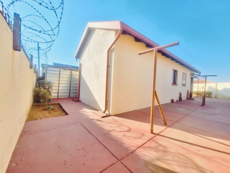 Rear exterior view of the property featuring a paved courtyard, perimeter wall with razor wire, and a metal storage shed.