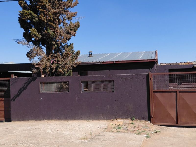 Front exterior view of the property featuring a solid perimeter wall, metal gates, and a corrugated metal roof structure.