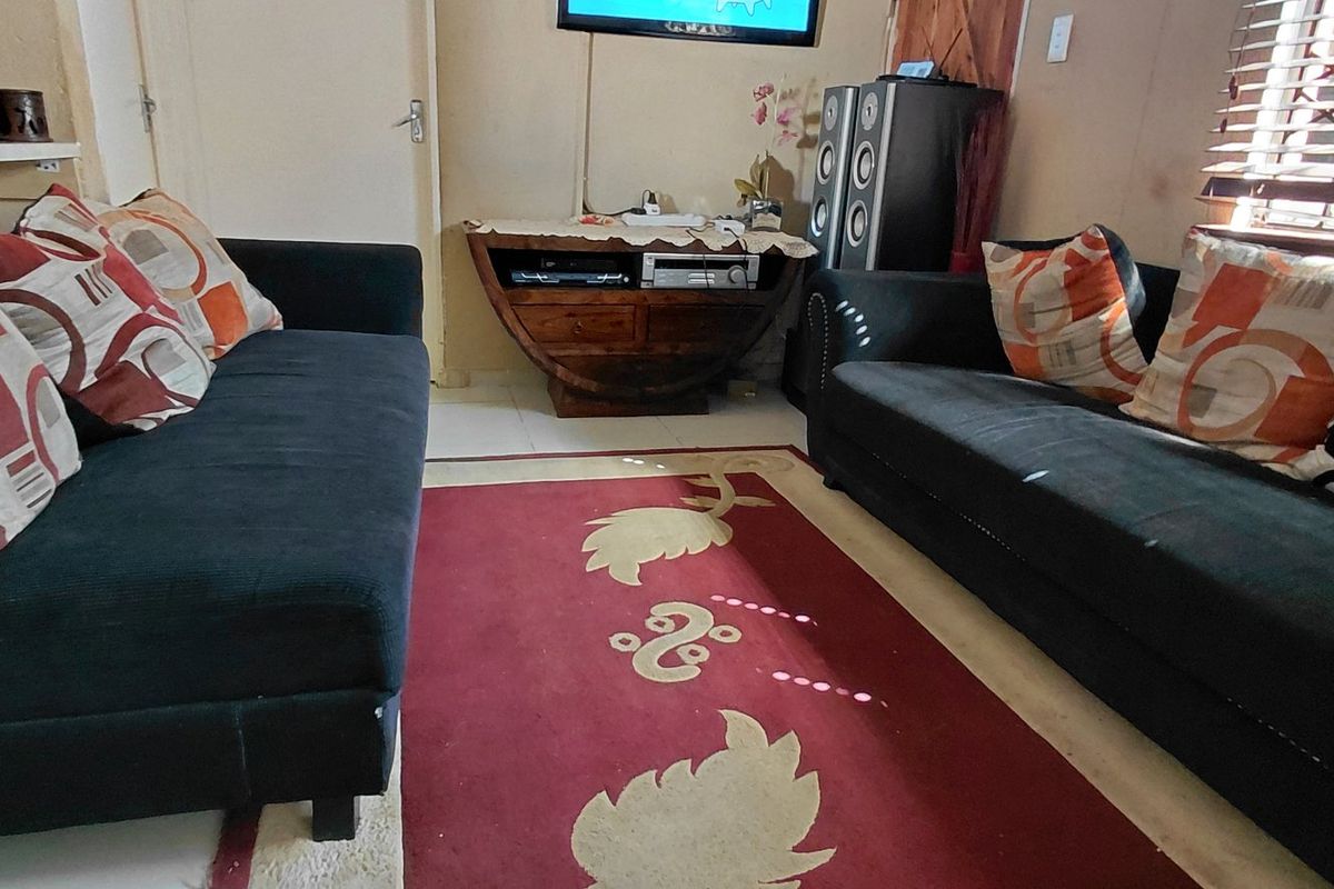 A compact living room featuring tiled flooring and venetian blinds, currently furnished with seating and media equipment.