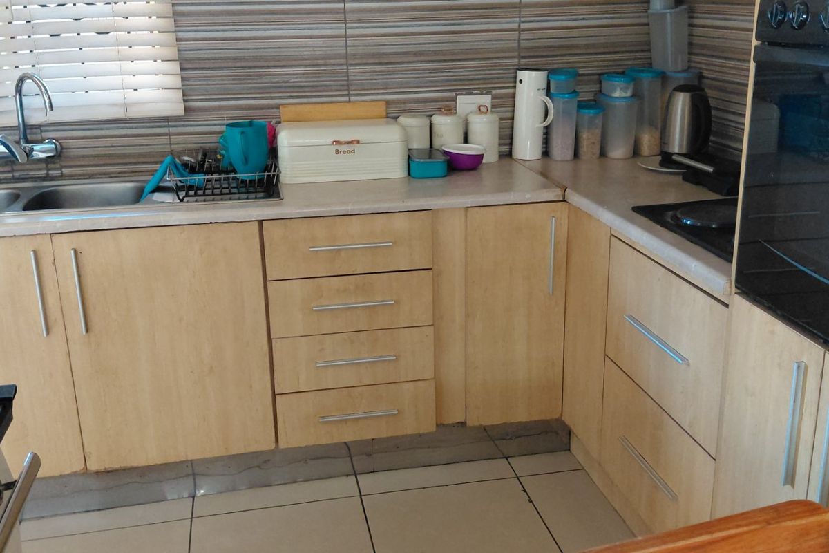 A functional kitchen featuring light wood-finish cabinetry, a double basin sink, tiled splashbacks, and a built-in oven.