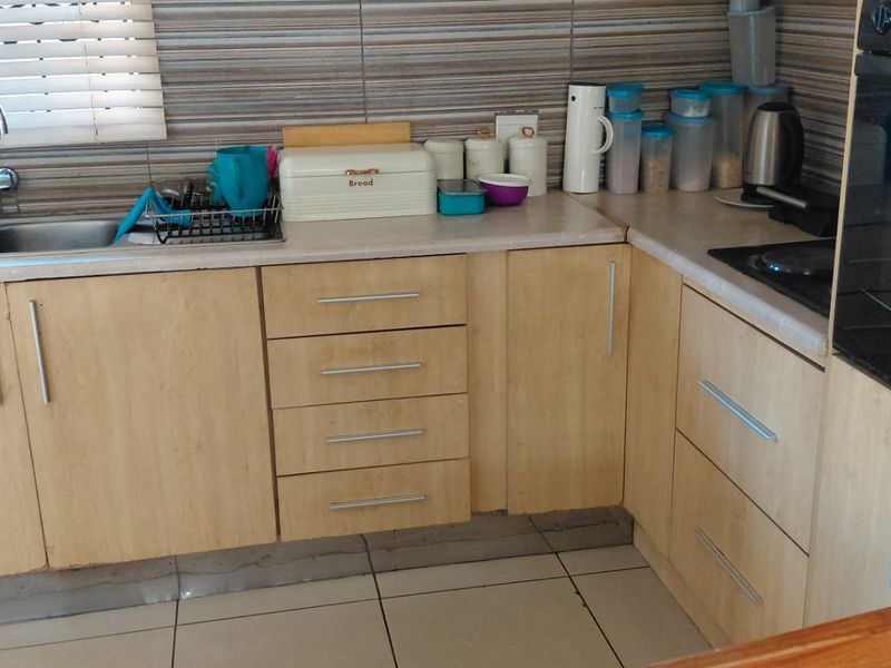 A functional kitchen featuring light wood-finish cabinetry, a double basin sink, tiled splashbacks, and a built-in oven.