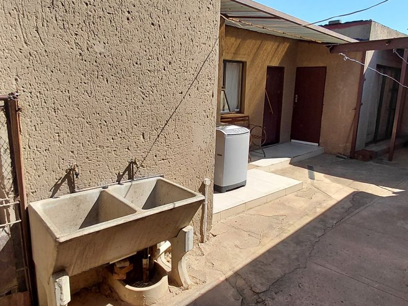 Rear exterior area featuring a concrete laundry trough, paved patio space, and covered walkway access to the main dwelling.