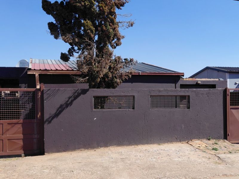 Front view of the property featuring a dark perimeter wall, metal security gates, and a corrugated metal roof structure.