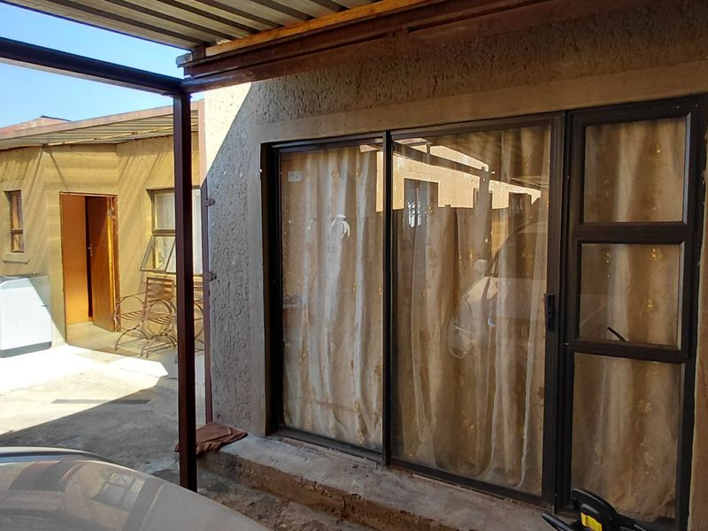 A covered outdoor patio area featuring a metal roof structure, concrete paving, and a sliding glass door entrance to the main dwelling.