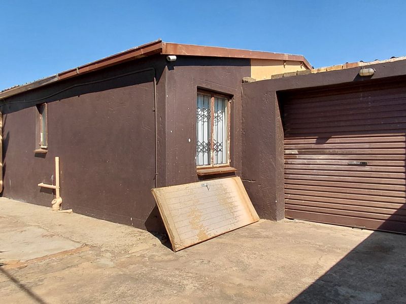 Front exterior view of the property featuring a roller garage door, security bars on windows, and a concrete driveway area.
