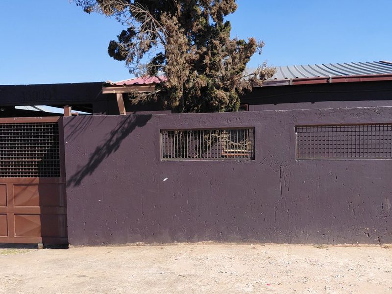 Front exterior view of the property featuring a solid perimeter wall with integrated security gates and grilles, and a corrugated metal roof structure.
