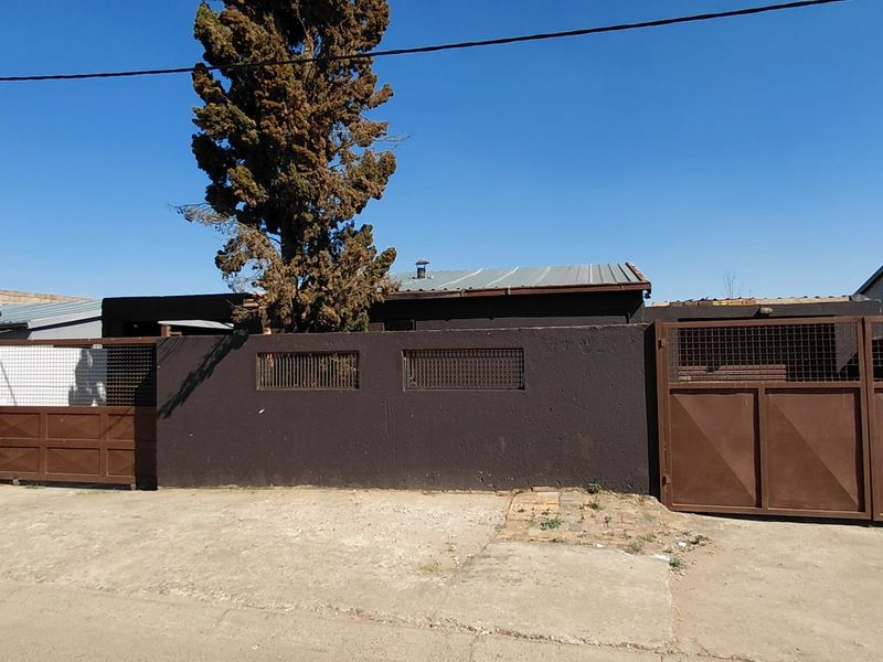 Front exterior view of the property featuring a solid perimeter wall, metal gates, and a concrete driveway leading to the main entrance.