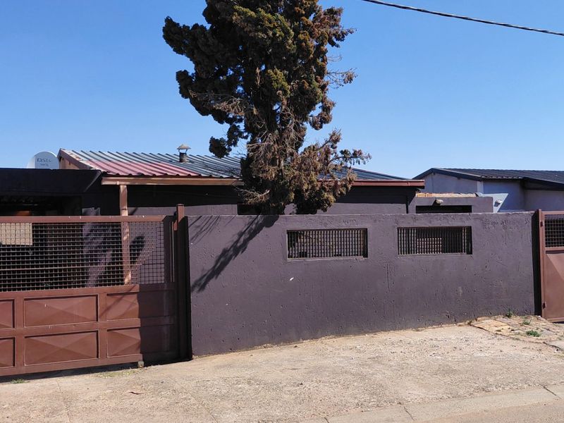 Front exterior view of the property featuring a solid perimeter wall, metal security gates, and a corrugated metal roof.