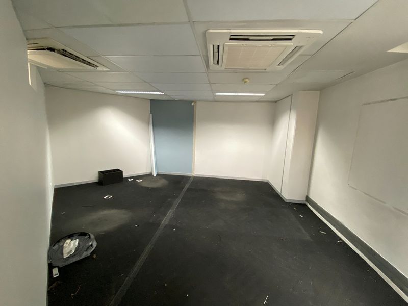 An empty commercial office space featuring a suspended ceiling with integrated air conditioning and dark carpeting, suitable for a variety of business uses.