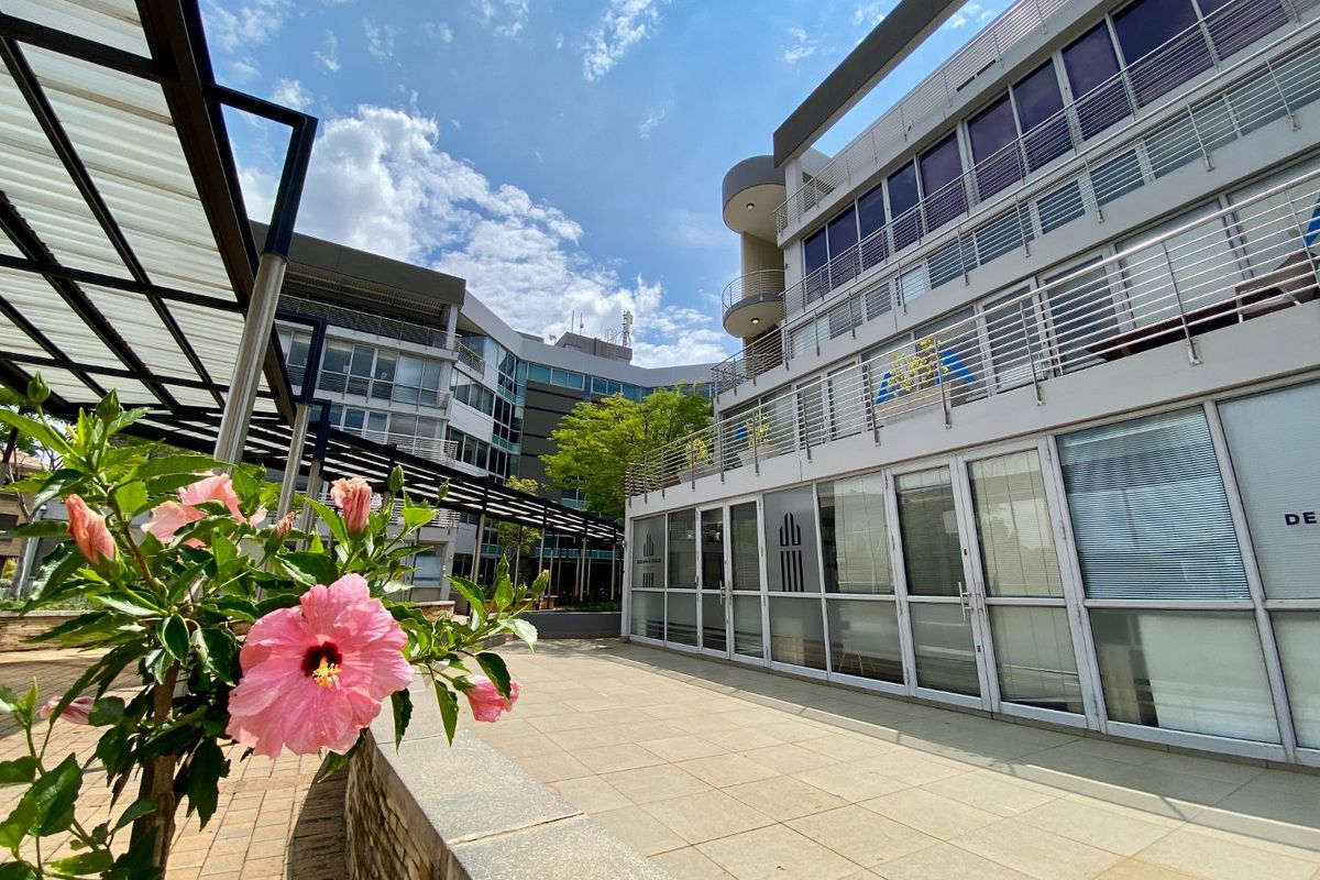 A modern commercial building exterior featuring a paved terrace, metal pergola structure, and multi-story glass facade with stainless steel balcony railings.