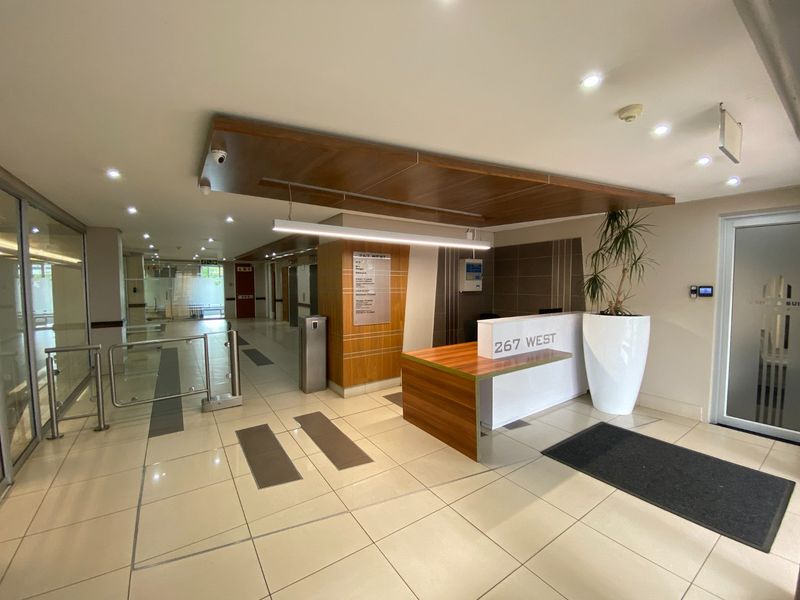 Modern commercial building lobby featuring a reception desk, wood veneer accents, tiled flooring, and secure access turnstiles.