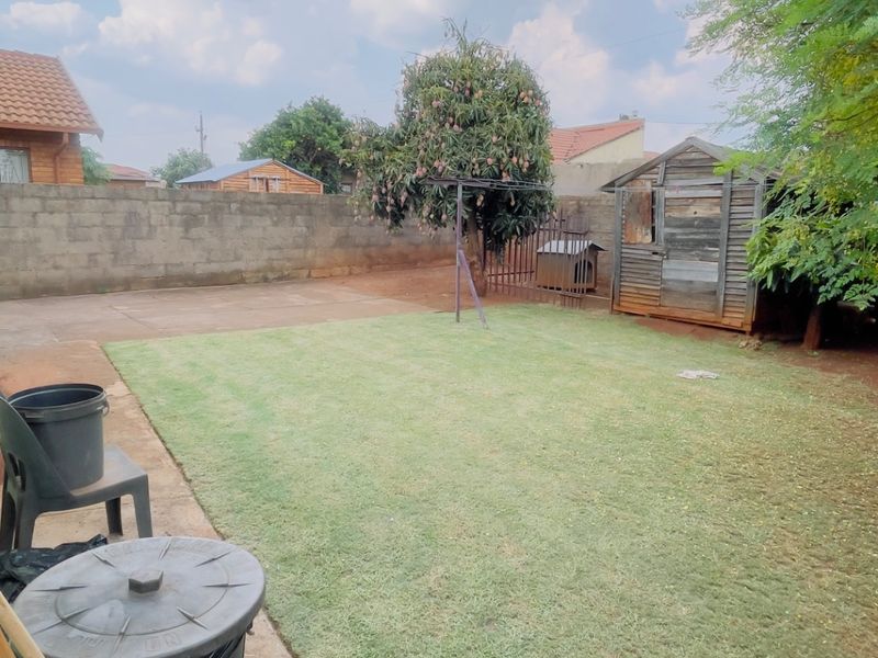 A private backyard featuring a lawn, paved patio area, and a wooden storage shed enclosed by a perimeter wall.