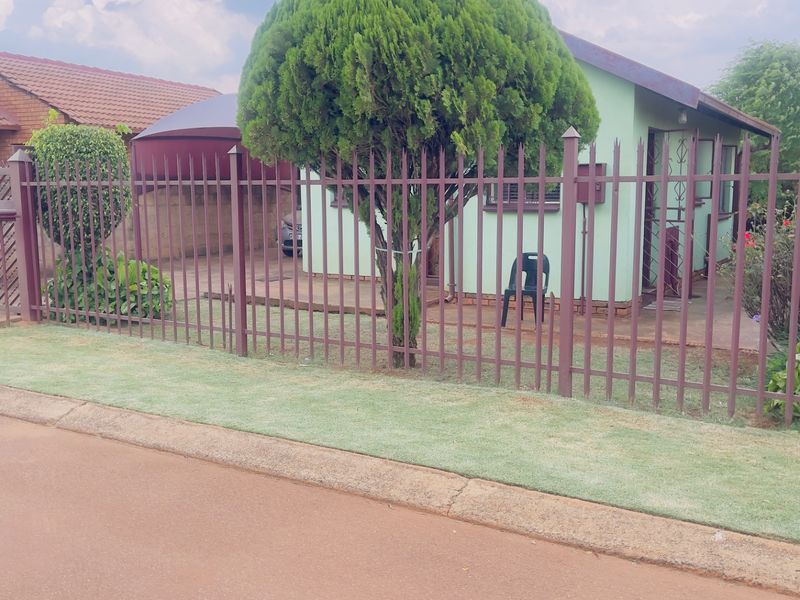 Front view of the property featuring a metal perimeter fence, gated driveway, and a covered carport area.