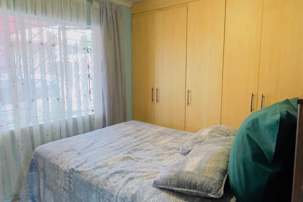 A bedroom featuring built-in wooden cupboards, tiled flooring, and a window fitted with security bars.