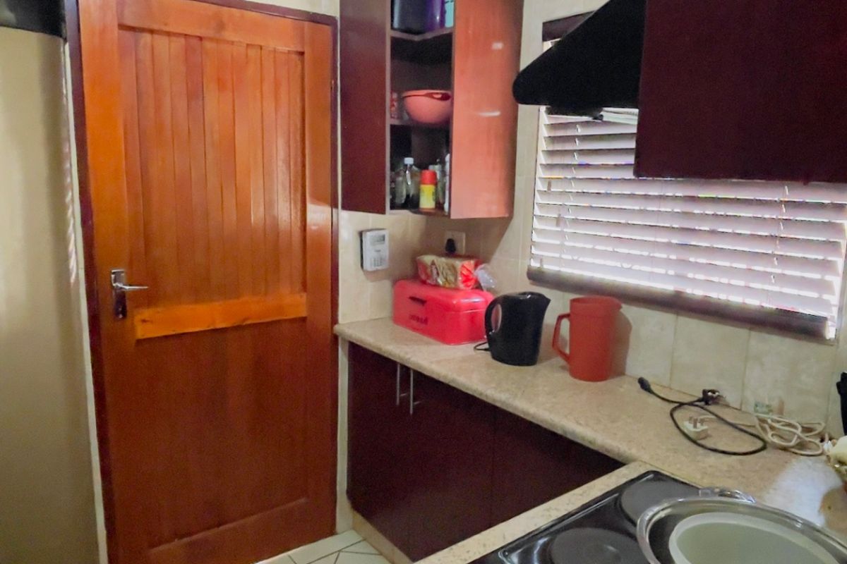 Compact kitchen featuring dark wood cabinetry, laminate countertops, an electric hob with extractor fan, and tiled flooring.
