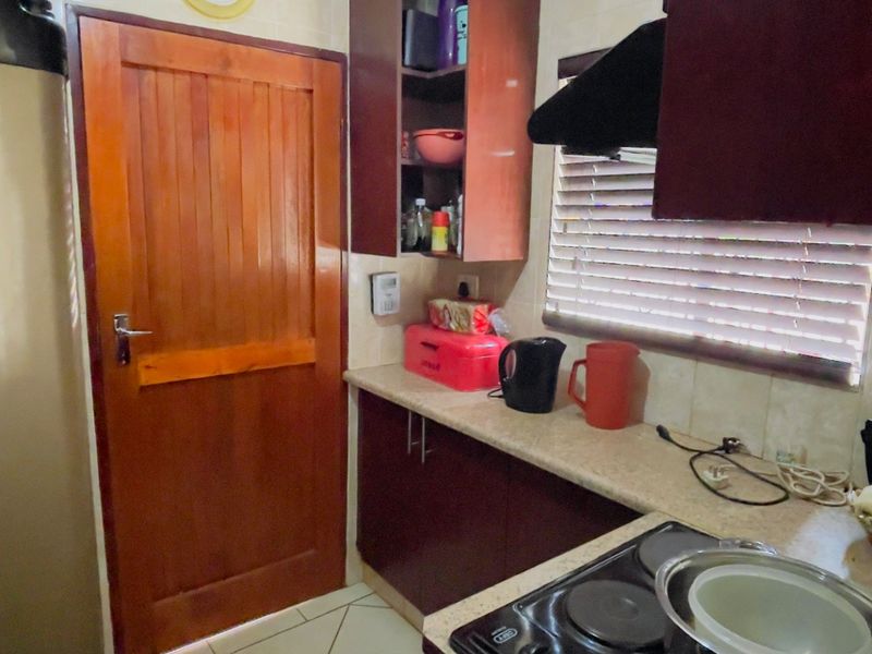Compact kitchen featuring dark wood cabinetry, laminate countertops, an electric hob with extractor fan, and tiled flooring.