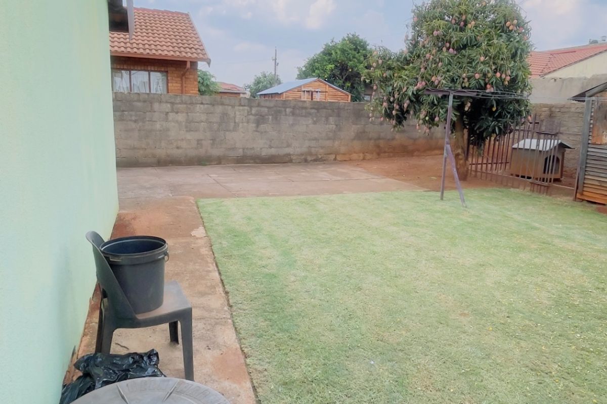 A rear garden area featuring a lawn, concrete paving, and a perimeter boundary wall.