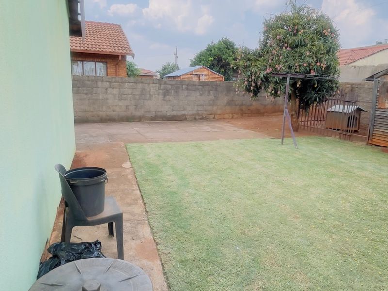 A rear garden area featuring a lawn, concrete paving, and a perimeter boundary wall.