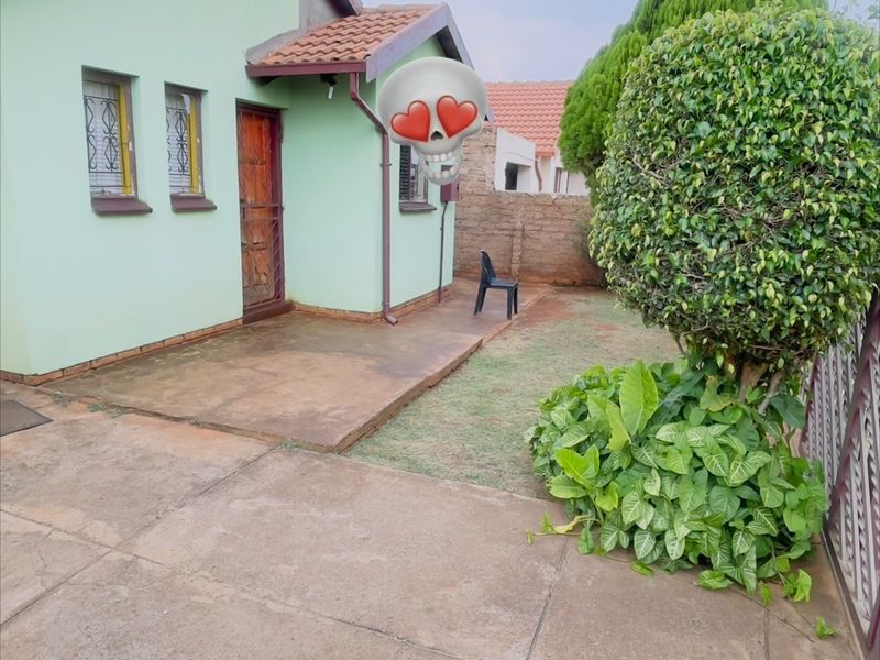 Front view of a single-story house featuring a concrete driveway, tiled roof, and a small garden area with boundary walling.