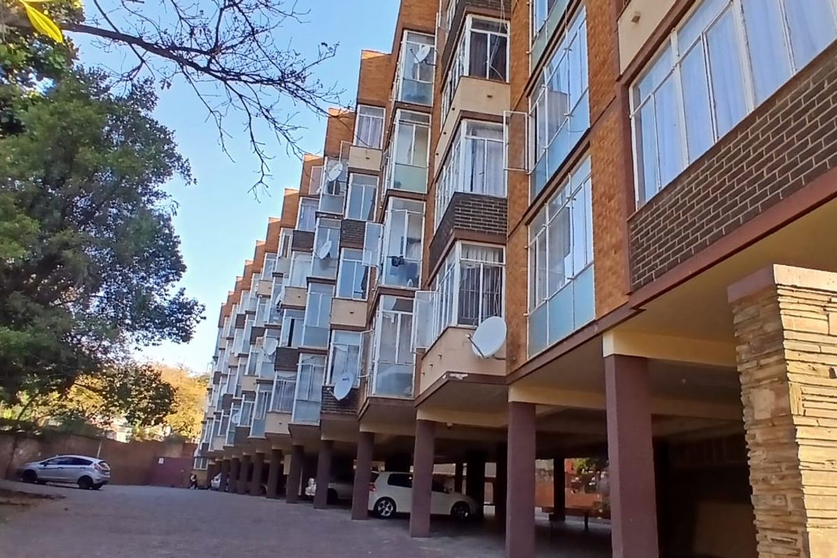 Exterior view of a multi-story residential apartment building featuring brick facade, covered ground-level parking, and stone-clad structural pillars.