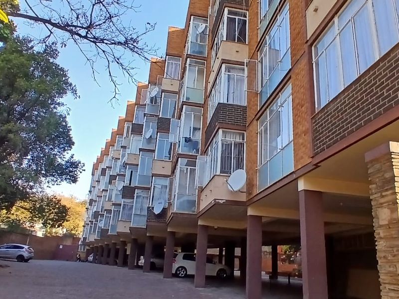 Exterior view of a multi-story residential apartment building featuring brick facade, covered ground-level parking, and stone-clad structural pillars.