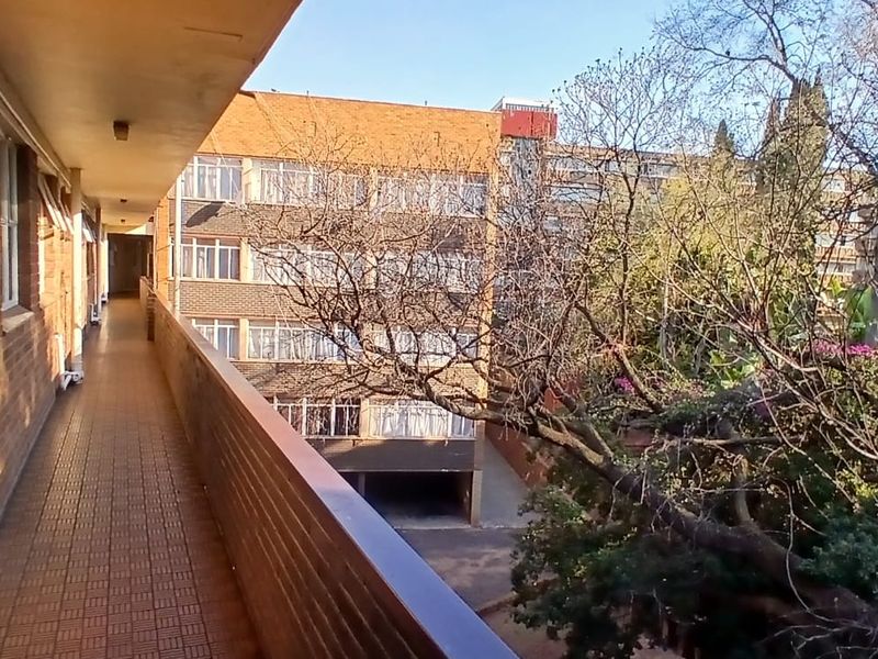 A covered exterior balcony with tiled flooring and brick wall finishes, overlooking a neighbouring building and mature trees.