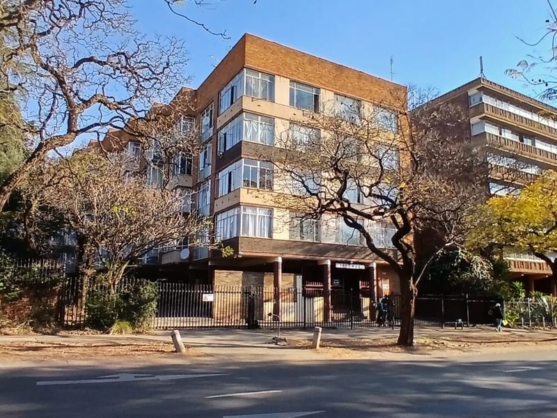 Street-level view of a multi-story residential apartment building featuring a brick facade and secure perimeter fencing.