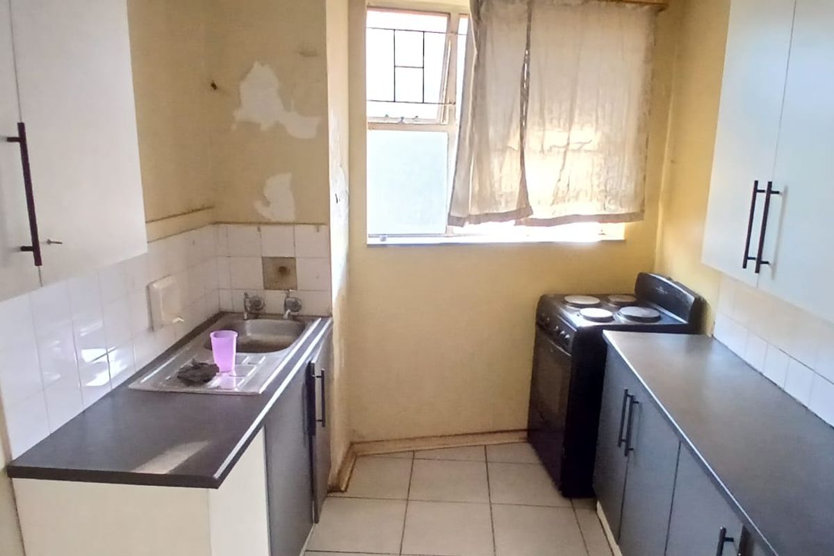A compact kitchen featuring built-in cabinetry, a stainless steel sink, and tiled flooring. The space requires cosmetic updates to the walls and finishes.
