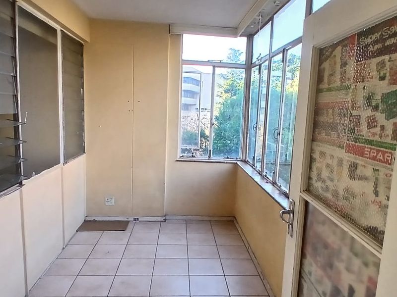An enclosed sunroom or patio area featuring tiled flooring and large windows, offering a bright space in need of cosmetic updates.