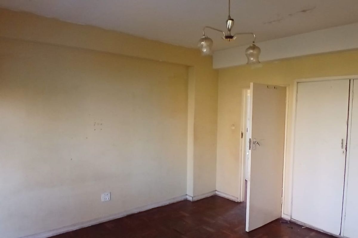 An empty bedroom featuring parquet flooring, built-in cupboards, and a ceiling light fixture, requiring cosmetic updates to the walls and ceiling.