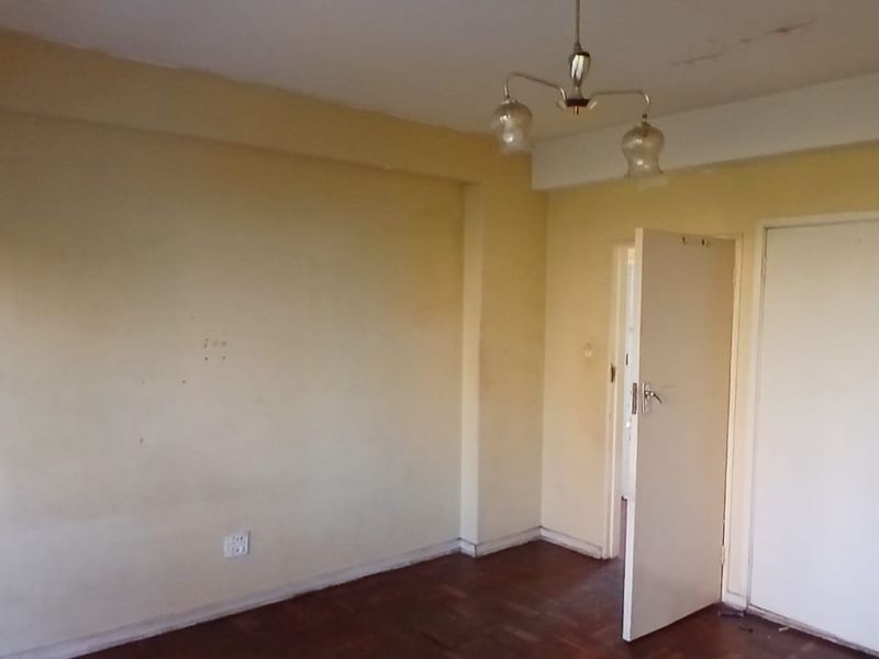 An empty bedroom featuring parquet flooring, built-in cupboards, and a ceiling light fixture, requiring cosmetic updates to the walls and ceiling.