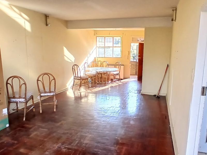 Spacious open-plan living and dining area featuring original parquet flooring and natural light, offering a blank canvas for renovation.