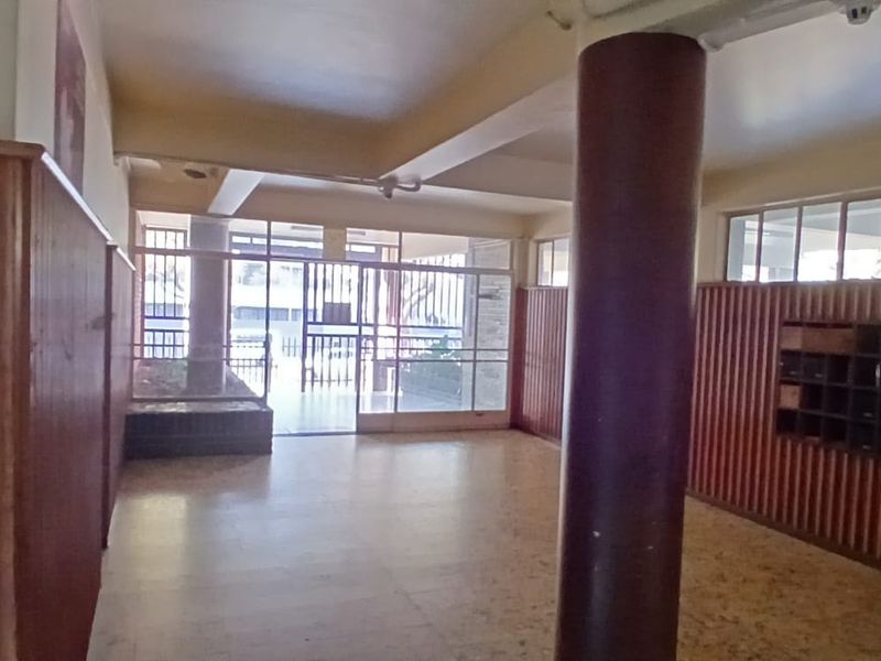 A spacious building entrance lobby featuring timber wall paneling, built-in mailboxes, a structural column, and terrazzo flooring leading to a glass entrance door.