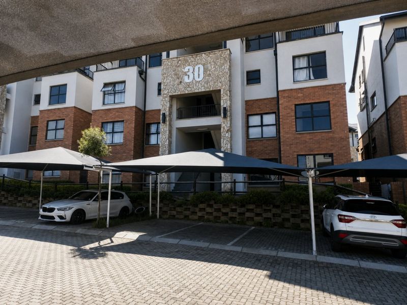 Front elevation of a multi-story apartment building featuring brick and stone facade, paved parking area, and covered shade cloth carports.