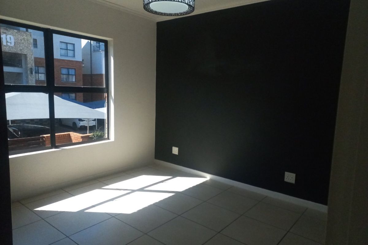 A bright, empty bedroom featuring neutral tiled flooring, a striking black accent wall, and a modern circular ceiling light fixture.
