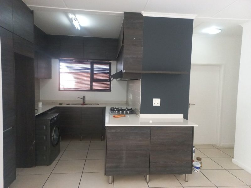 Modern kitchen featuring dark wood cabinetry, stone countertops, a gas hob, extractor fan, and tiled flooring in an open-plan layout.