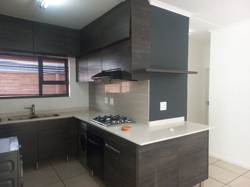 Modern kitchen featuring dark wood cabinetry, stone countertops, gas hob, extractor fan, and tiled backsplash. The space is clean and ready for use.
