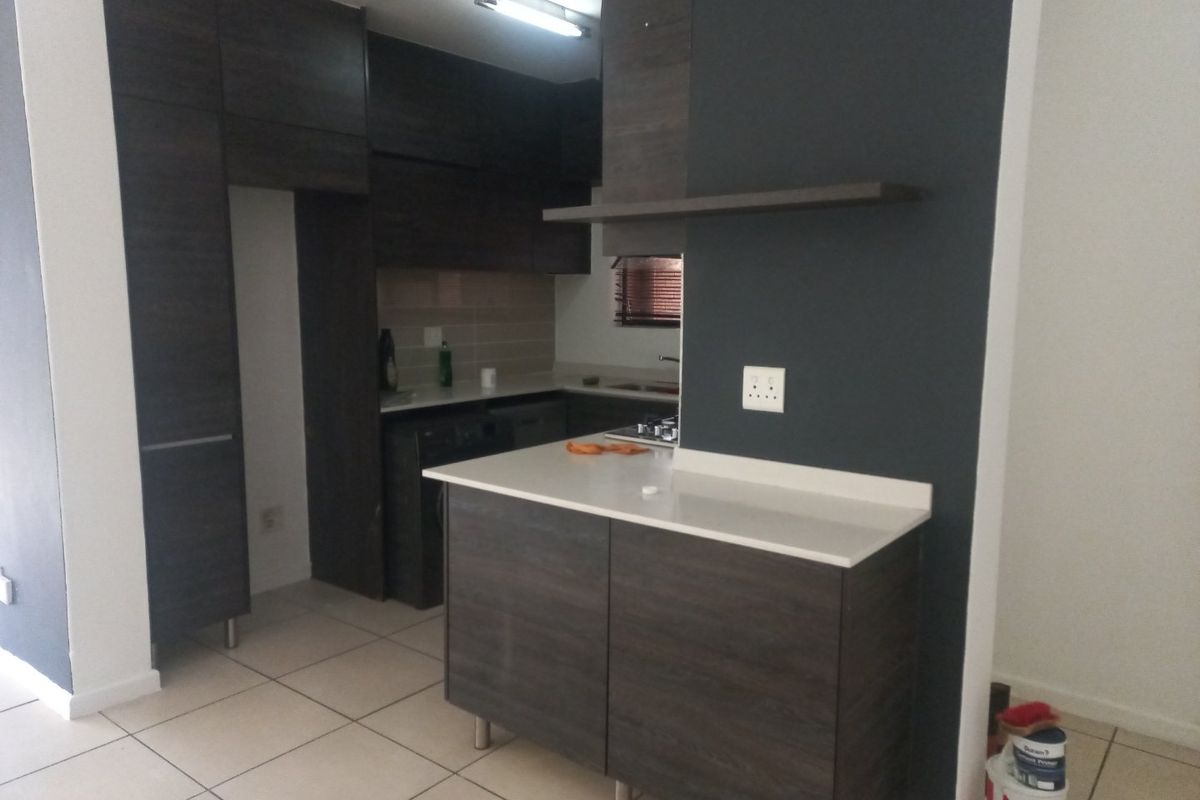 Modern kitchen featuring dark wood cabinetry, stone countertops, a central island, and tiled flooring, offering a clean and functional workspace.