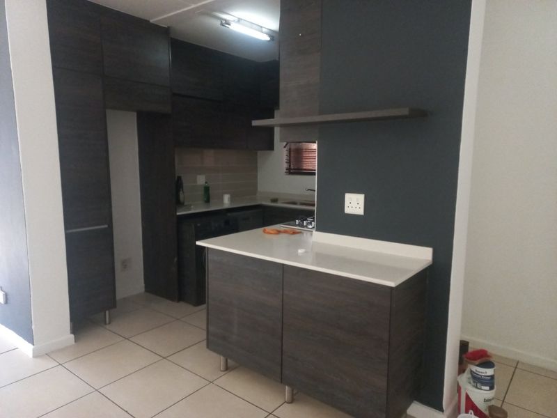 Modern kitchen featuring dark wood cabinetry, stone countertops, a central island, and tiled flooring, offering a clean and functional workspace.