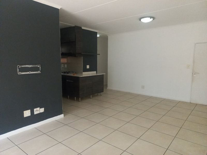An open-plan living and kitchen area featuring tiled flooring, dark cabinetry, and a built-in hob, offering a clean and functional space.