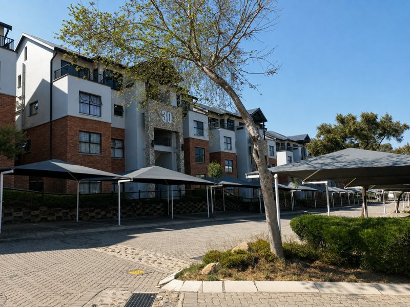 Exterior view of a multi-story apartment complex featuring brick and plaster facade, stone accents, and dedicated shade cloth parking bays.