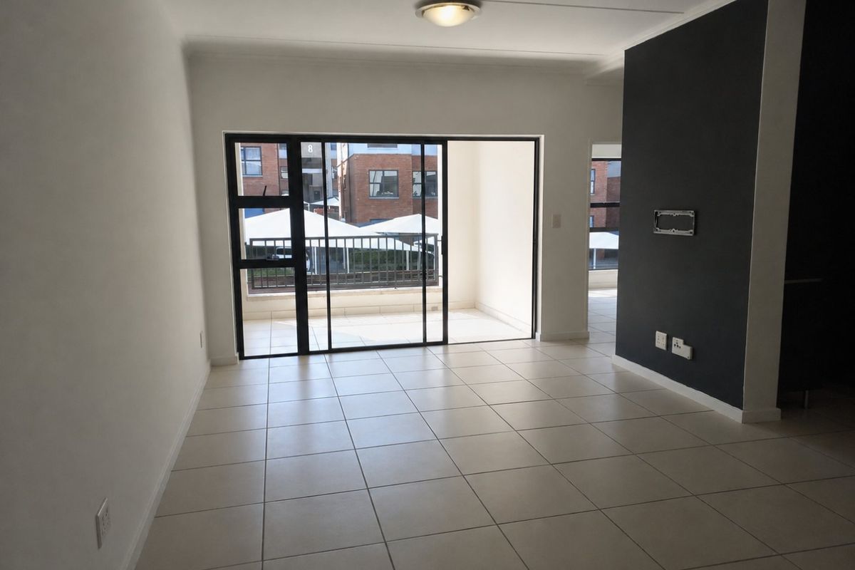 An empty, well-maintained living area featuring neutral tiled flooring, a dark accent wall, and a sliding glass door leading to a balcony.