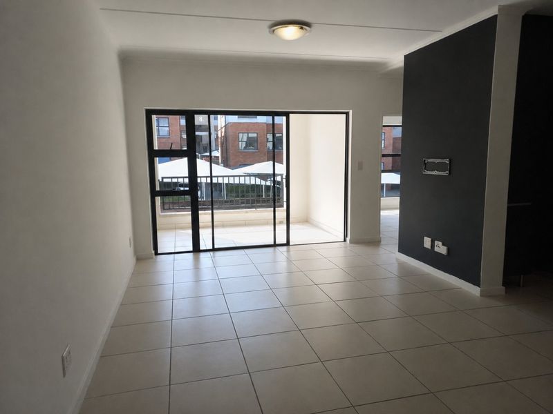 An empty, well-maintained living area featuring neutral tiled flooring, a dark accent wall, and a sliding glass door leading to a balcony.