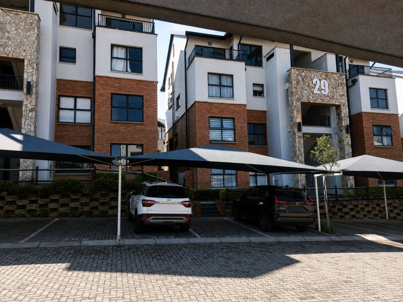 Exterior view of a modern apartment complex featuring brick and stone facade, balconies, and covered parking bays.
