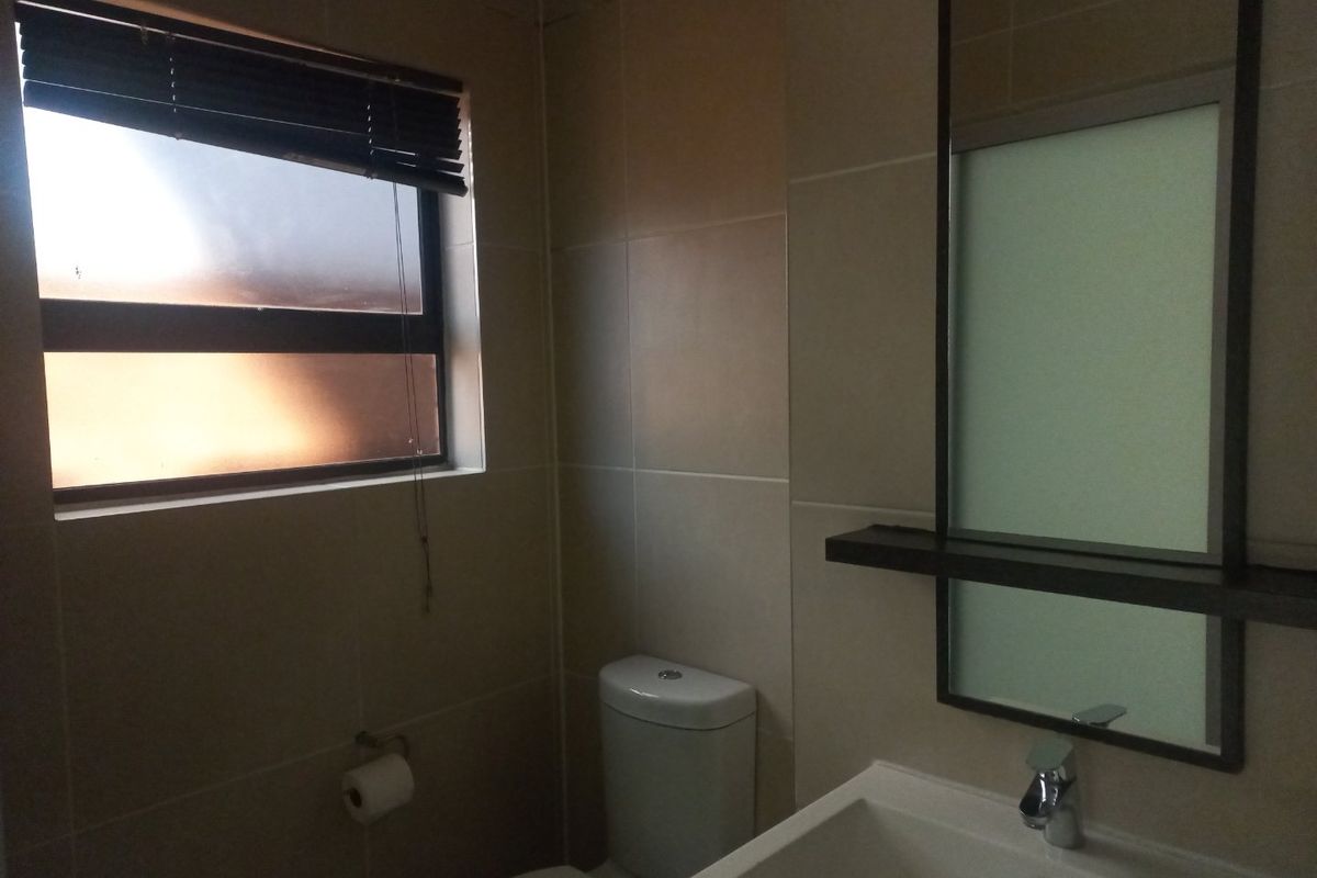 A clean, modern bathroom featuring tiled walls, a vanity basin with a mixer tap, a wall-mounted mirror, and a toilet.