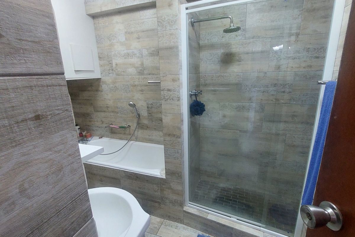 Modern bathroom featuring a combined bathtub and separate glass-enclosed shower with rainfall shower head, finished with neutral-toned wall and floor tiles.