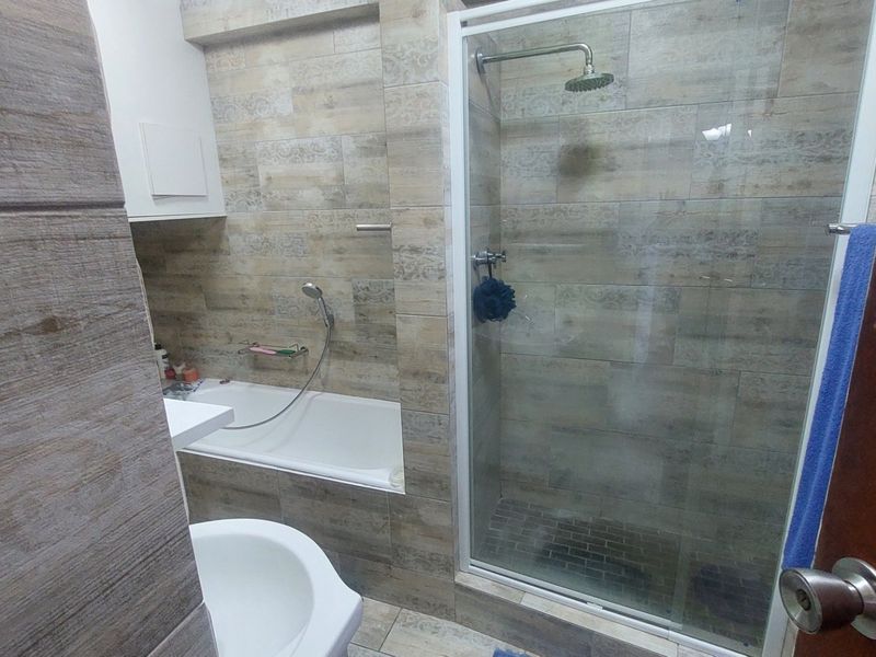 Modern bathroom featuring a combined bathtub and separate glass-enclosed shower with rainfall shower head, finished with neutral-toned wall and floor tiles.